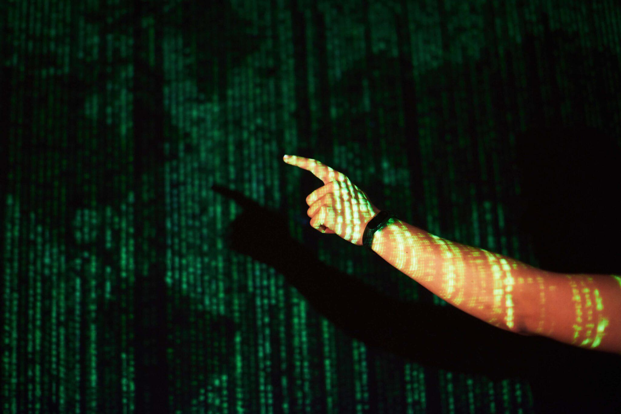 יד מצביעה על רקע של נתונים דיגיטליים בירוק, המסמלים טכנולוגיה וסייבר